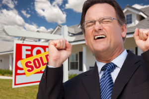 Excited Man in Front of Sold Real Estate Sign and Beautiful New House.